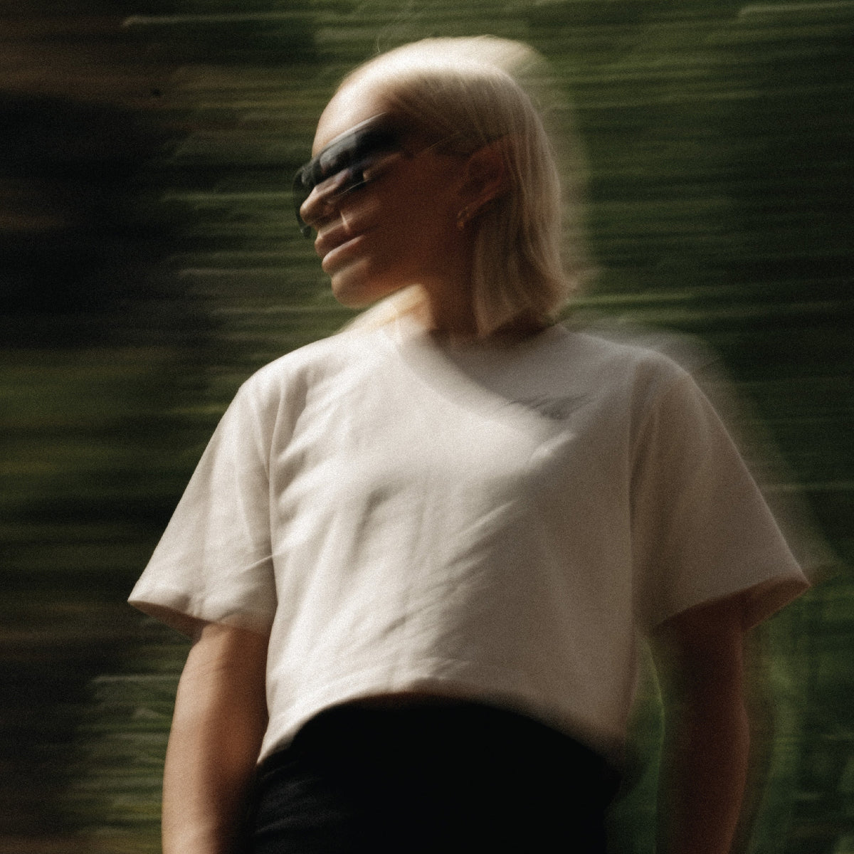 Person wearing a white t-shirt and sunglasses with a blurred green background