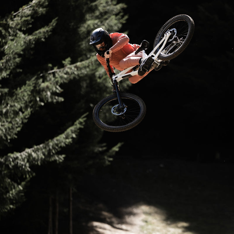Person on a bicycle in mid-air over a dirt jump with trees in the background