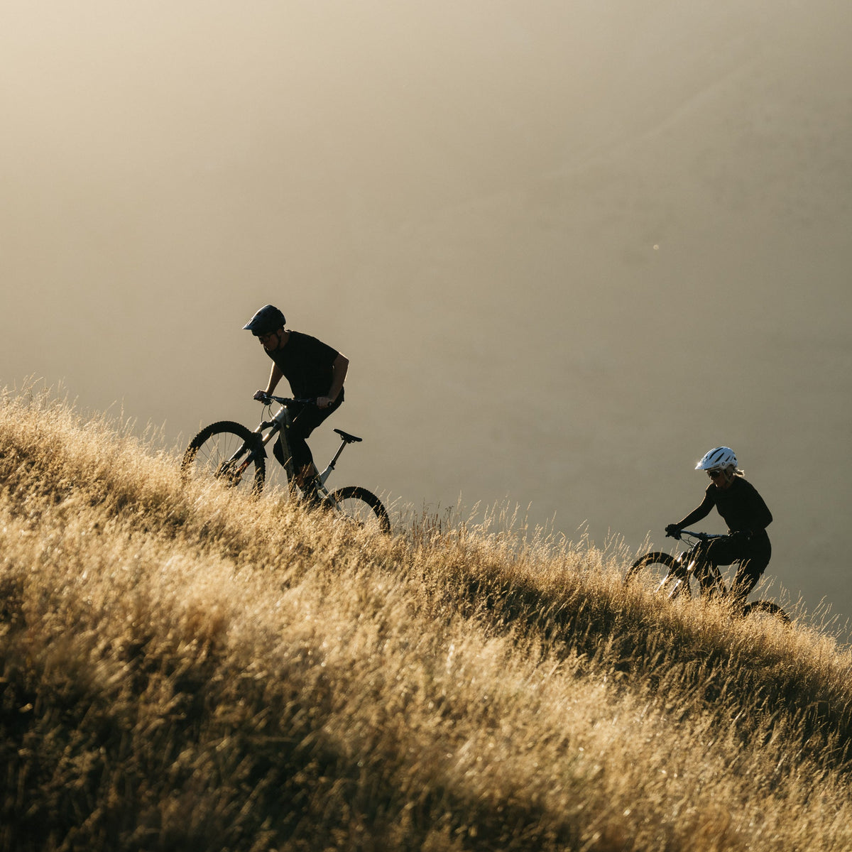 Two cyclists on a hill with a plain background