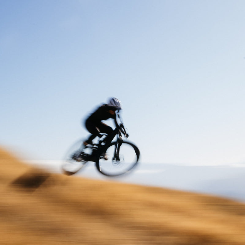 Person riding a bicycle on a hill with a clear sky