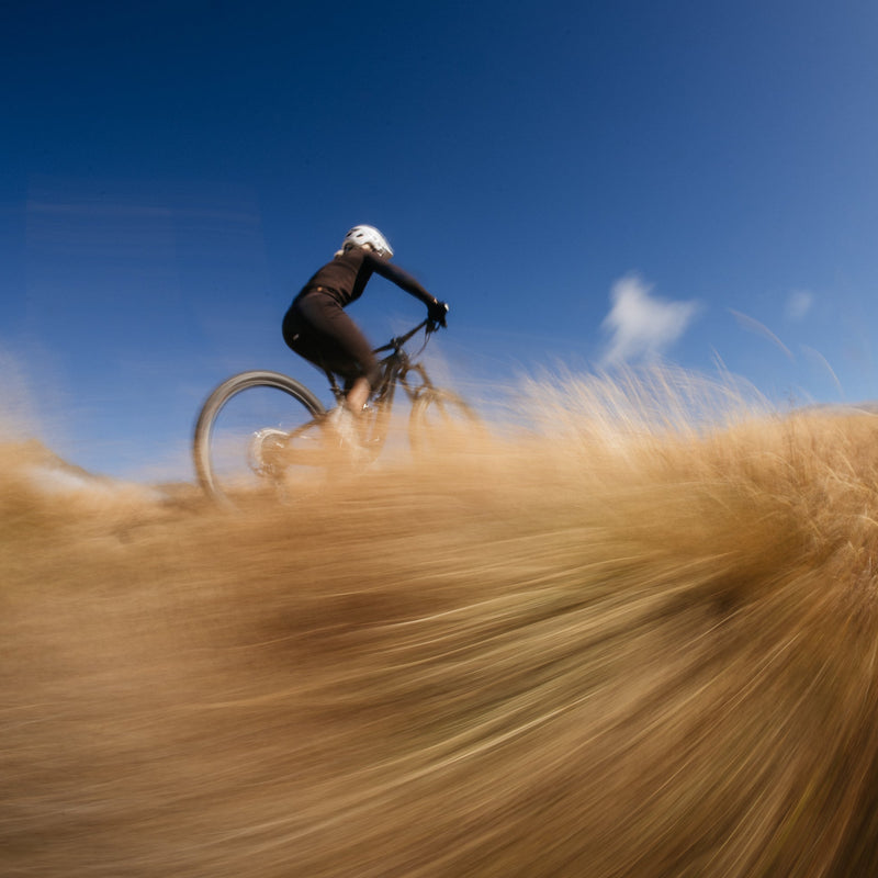 Person riding a bicycle on a dirt path with a blue sky in the background