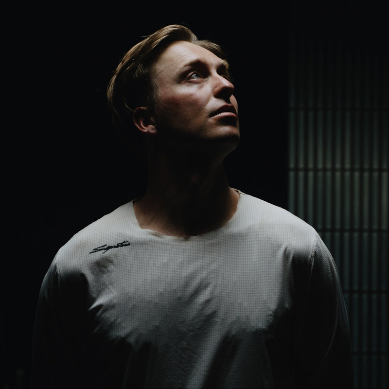 Man wearing a gray t-shirt in a dark room with a textured wall.