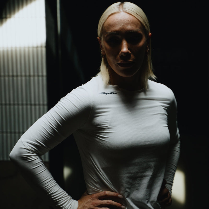 Person wearing a fitted white long-sleeve shirt in a dimly lit room.