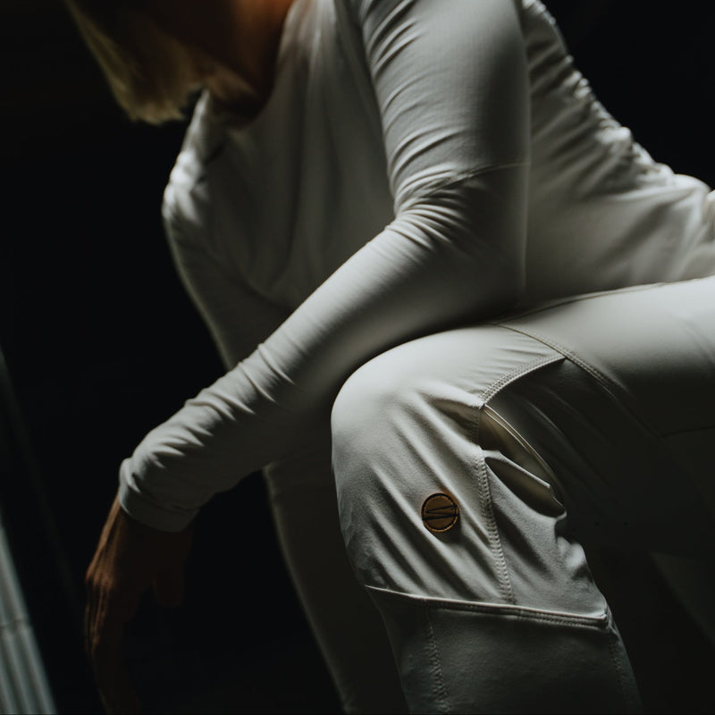 Person wearing a white long-sleeve top and light-colored pants in a dimly lit setting