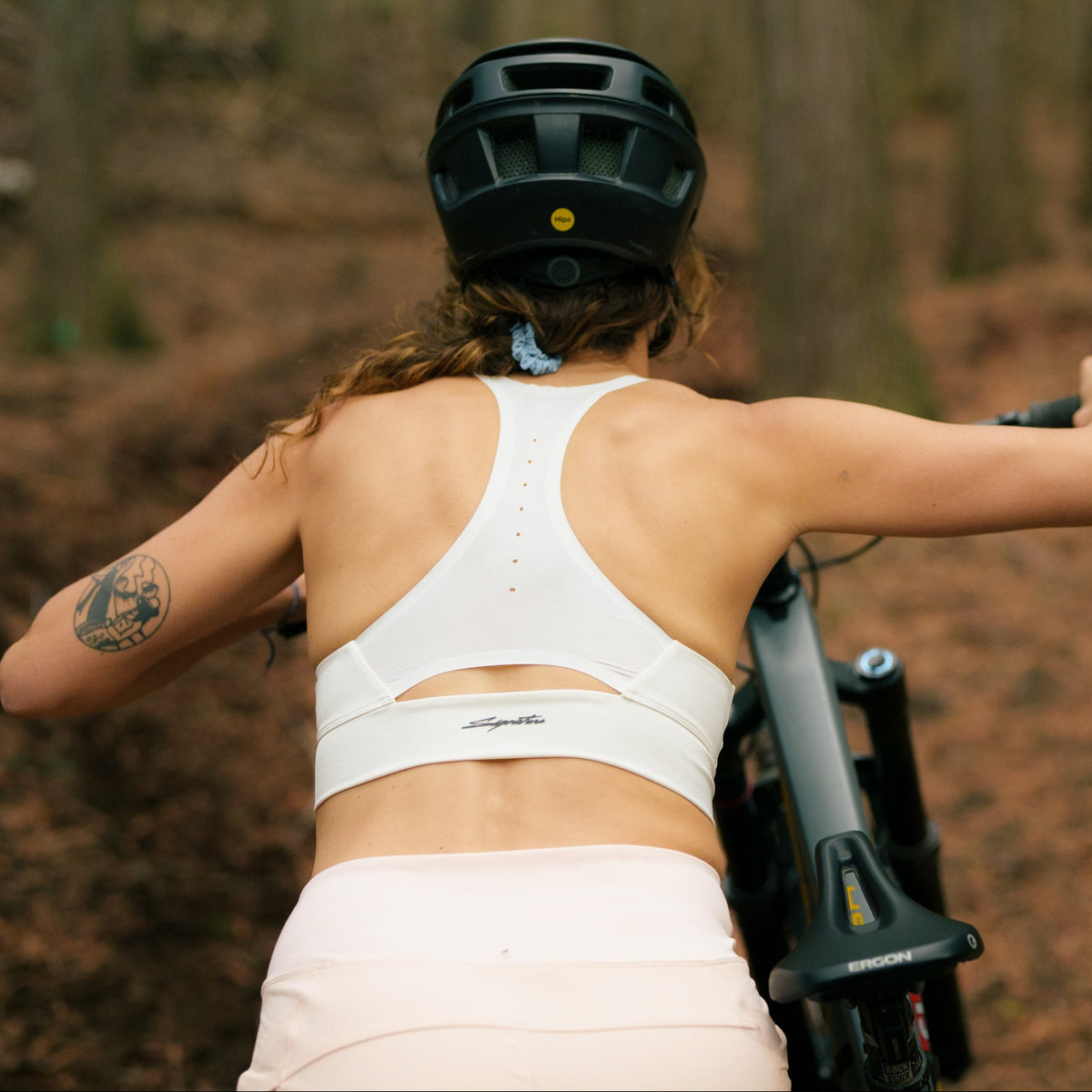 woman pushing her mountain bike through a forest wearing signature ride bra