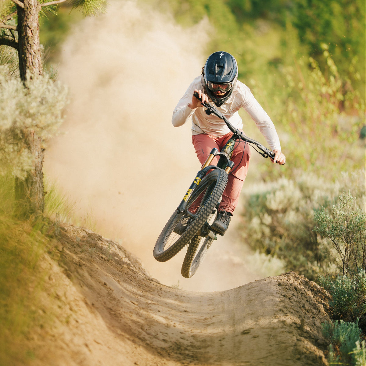 Person riding a mountain bike on a dirt trail with trees and greenery in the background