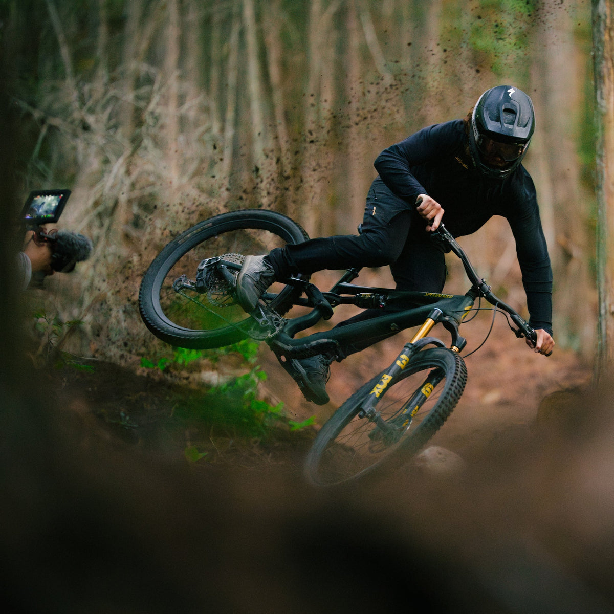 mountain biker spraying dirt while riding off a jump with a filmer in the background getting the shot